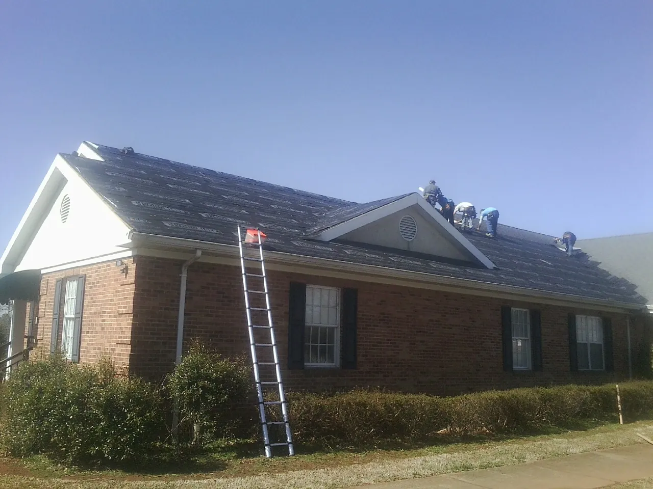 Crew tearing shingles off a brick ranch roof with a ladder set — Emergency Roof Repair work by our crew in Jordan