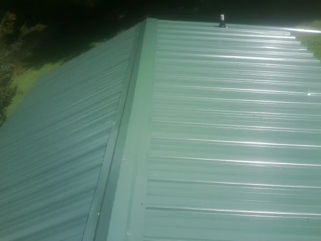 New green metal panels meeting at the ridge of a roof — Flat Roof Repair work by our crew in Jordan