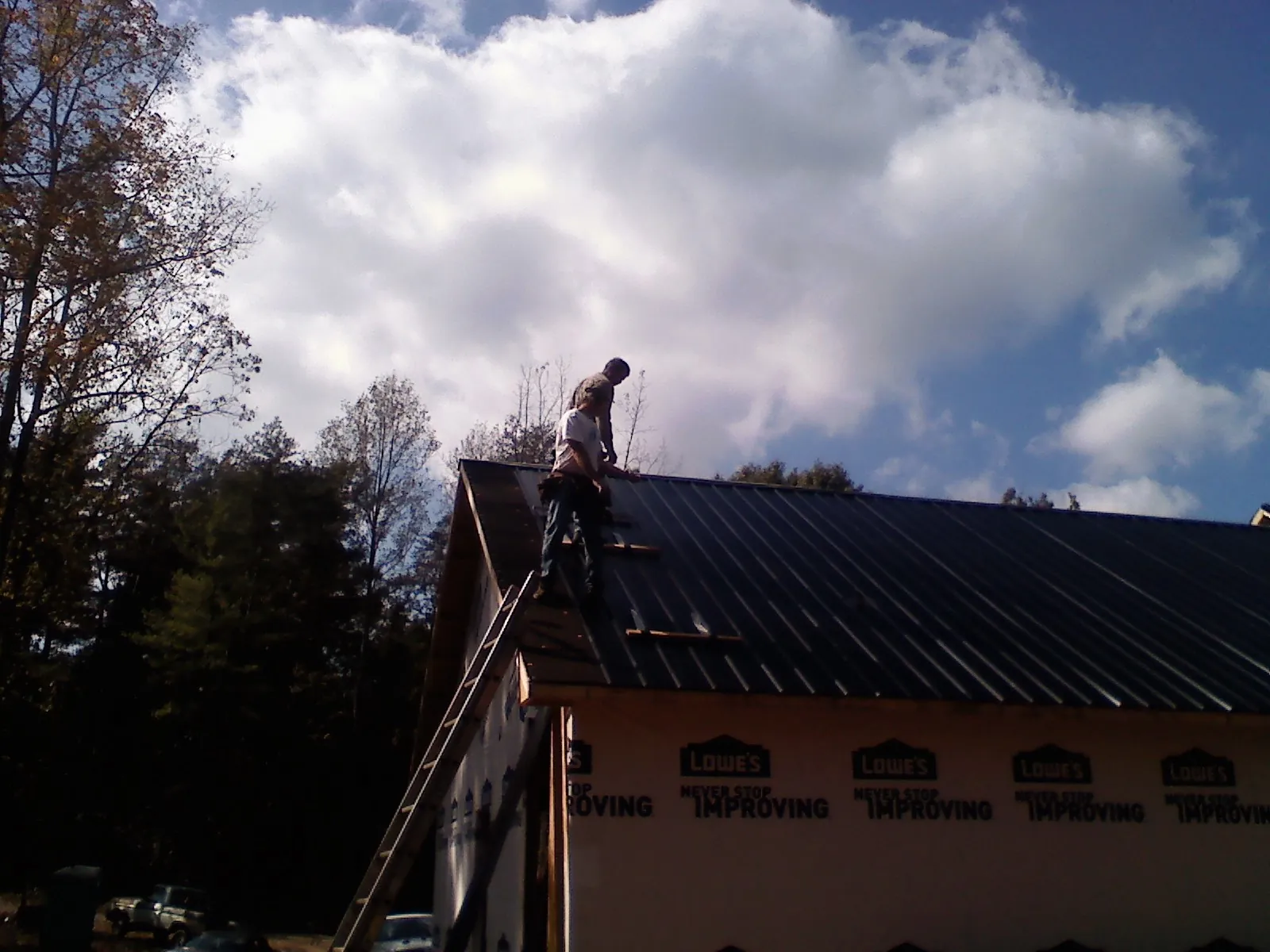 Roofer fastening dark metal panels high against a cloudy sky, from a Roof Inspection job in Jordan